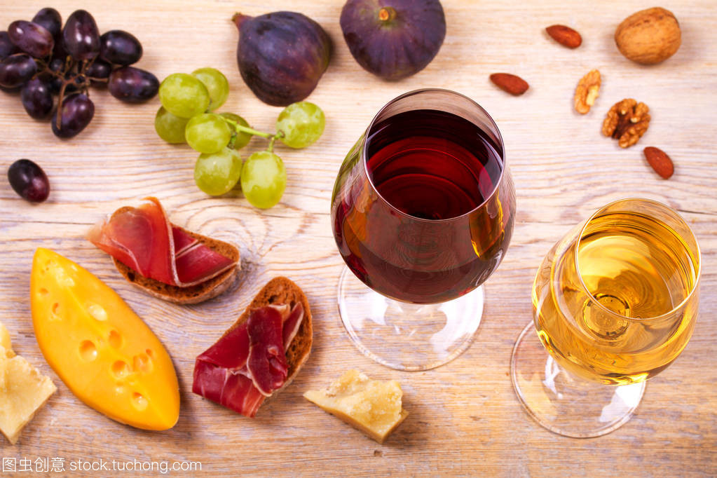 紅色和白色奶酪、 火腿、 無花果和葡萄與葡萄酒杯。木制的桌子上的酒杯。葡萄酒的靜物